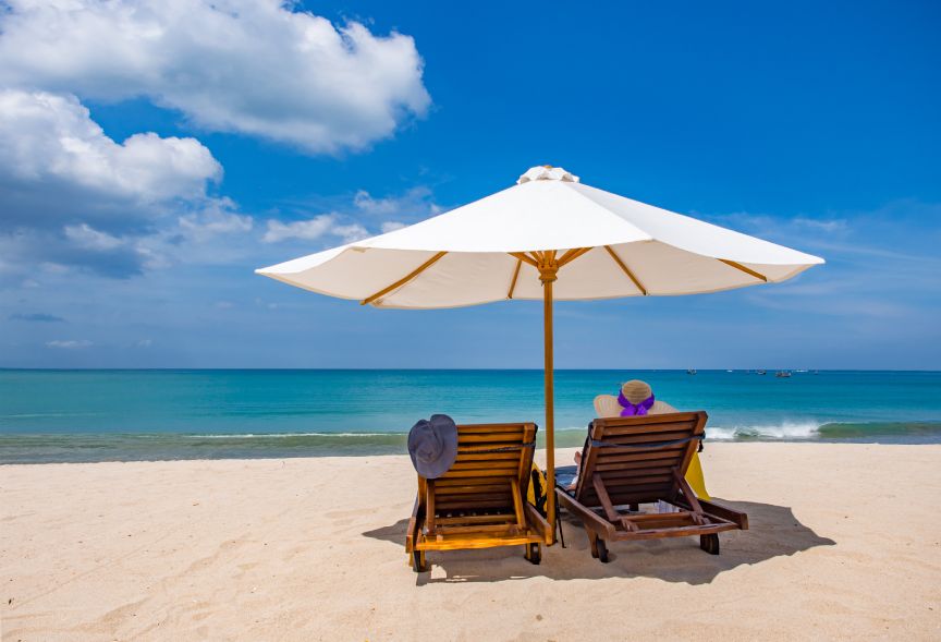 woman resting under a beach umbrella facing the ocean in a deserted beach with deep blue sky